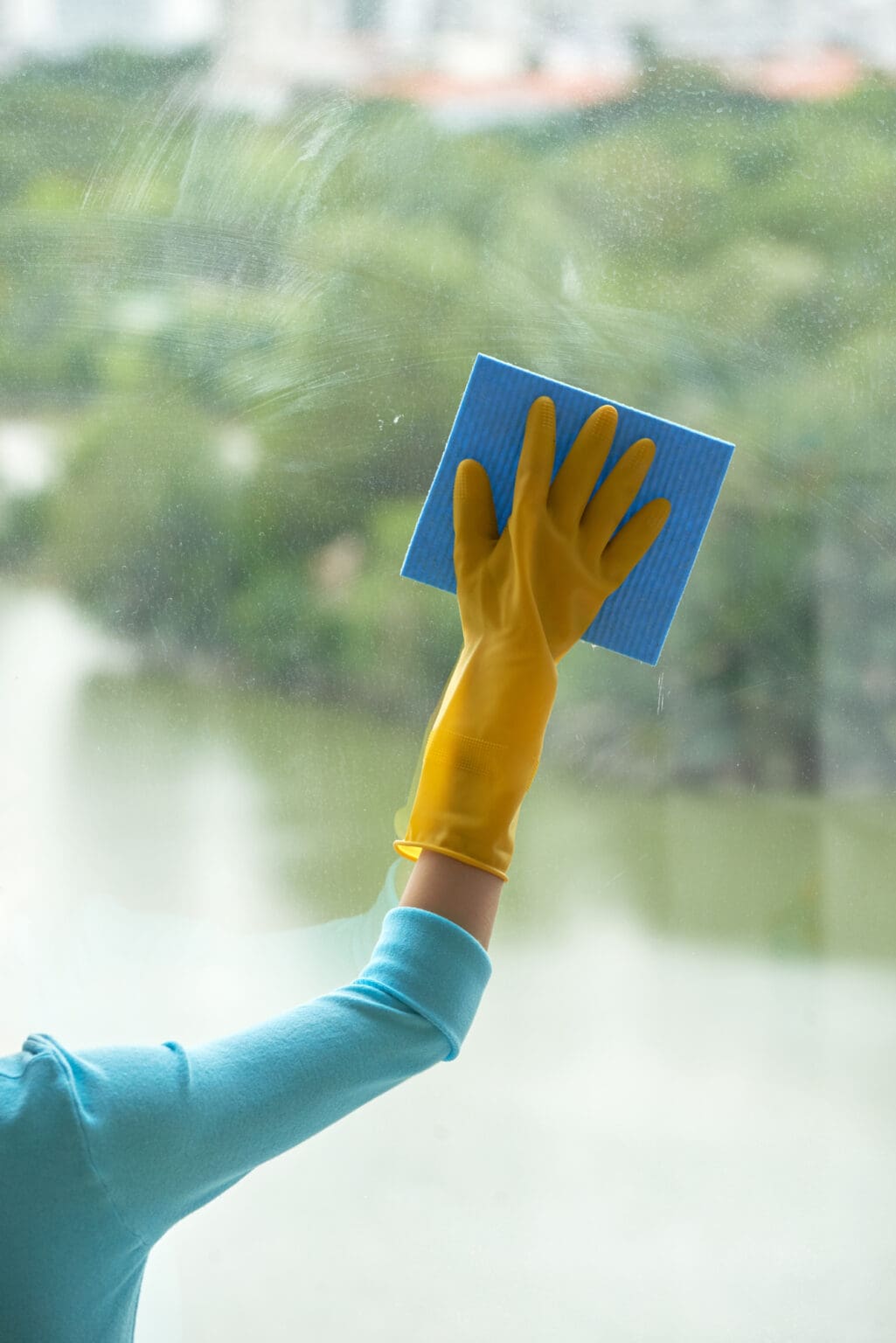Close-up shot of unrecognizable woman wearing rubber gloves cleaning panoramic window with help of rag